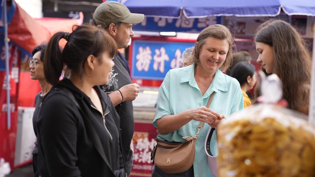 2026年2月4日，在海南海口骑楼老街，来自俄罗斯的游客在年货集市上选购干果。新华社记者 许雨深 摄 